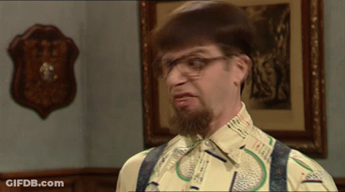 A Man With A Beard Wearing Glasses And Suspenders Looks At The Camera GIF