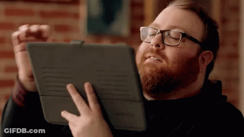 A Man With A Beard Wearing Glasses Is Holding A Tablet GIF