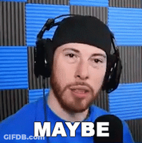 A Man With A Beard Wearing Headphones And A Blue Shirt Is Talking Into A Microphone . GIF