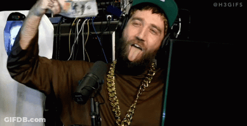 A Man With A Beard Wearing Headphones And A Gold Chain Sticks Out His Tongue GIF