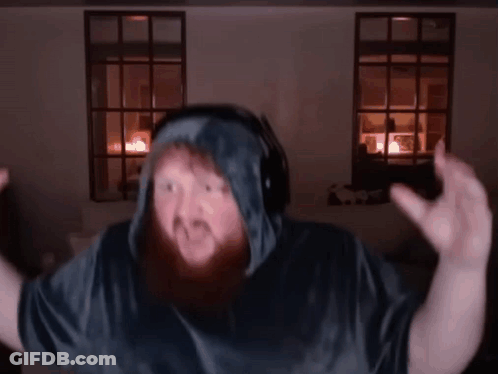 A Man With A Beard Wearing Headphones And A Hooded Shirt Is Dancing In A Dark Room . GIF
