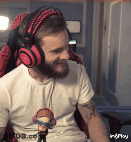 A Man With A Beard Wearing Headphones And Holding A Figurine That Says ' Imgplay ' On It GIF