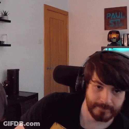 A Man With A Beard Wearing Headphones In Front Of A Paul Stan Poster GIF