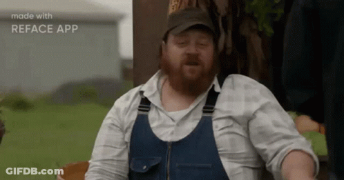 A Man With A Beard Wearing Overalls And A Hat Is Making A Funny Face . GIF