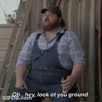 A Man With A Beard Wearing Overalls And A Plaid Shirt Is Sitting On A Ladder Holding A Beer . GIF