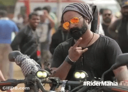 A Man With A Beard Wearing Sunglasses And A Beanie Is Giving The Middle Finger While Riding A Motorcycle . GIF