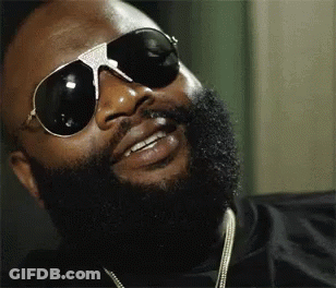 A Man With A Beard Wearing Sunglasses And A Necklace Is Smiling . GIF