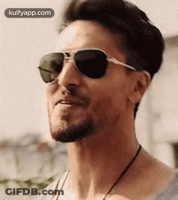 A Man With A Beard Wearing Sunglasses And A Necklace Is Smiling . GIF