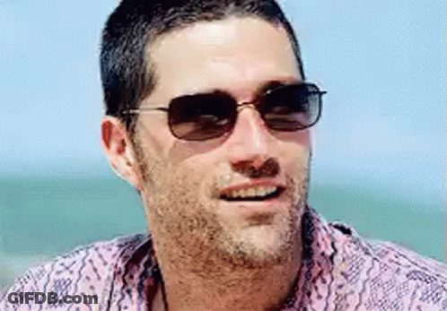A Man With A Beard Wearing Sunglasses And A Pink Shirt Is Smiling . GIF