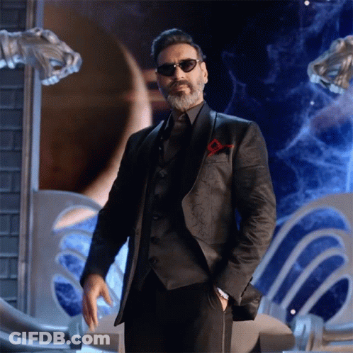A Man With A Beard Wearing Sunglasses And A Suit Stands With His Hands In His Pockets GIF