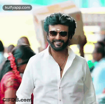 A Man With A Beard Wearing Sunglasses And A White Shirt Is Smiling In A Crowd . GIF