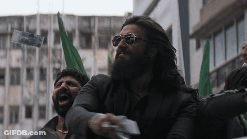 A Man With A Beard Wearing Sunglasses Holds A Piece Of Paper In His Right Hand GIF