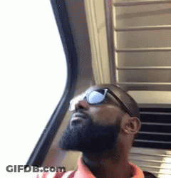 A Man With A Beard Wearing Sunglasses Is Looking Out A Window . GIF