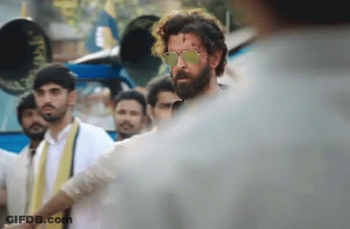 A Man With A Beard Wearing Sunglasses Is Standing In A Crowd GIF