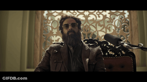 A Man With A Beard Wearing Sunglasses Sits In Front Of A Microphone GIF