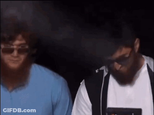 A Man With A Beard Wearing Sunglasses Stands Next To Another Man In A Blue Shirt GIF