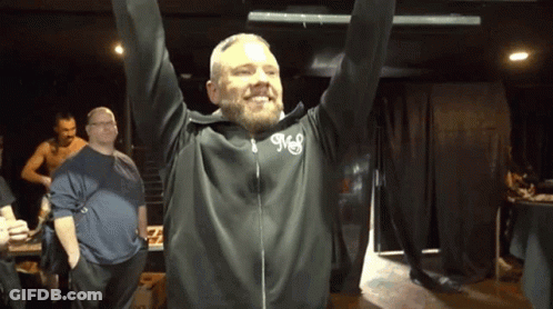 A Man With A Beard Wears A Black Jacket With The Letter M On The Front GIF