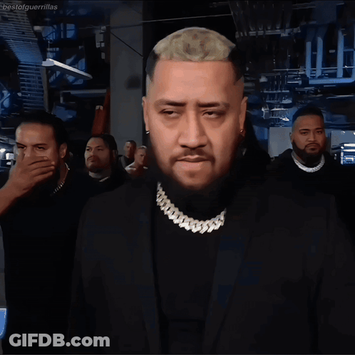 A Man With A Beard Wears A Black Suit And Gold Chain GIF