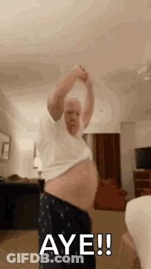 A Man With A Big Belly Is Dancing In A Living Room With His Shirt Off . GIF