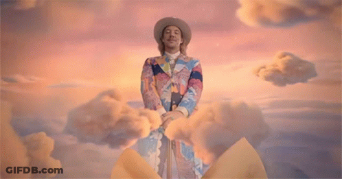 A Man With A Bow On His Head Stands Next To A Woman In A Yellow Dress GIF