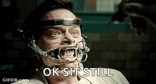 A Man With A Brace On His Teeth Is Sitting In A Chair And Says Ok Sit Still . GIF