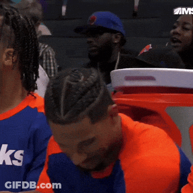 A Man With A Braided Hairdo Is Sitting In A Stadium Watching A Game GIF