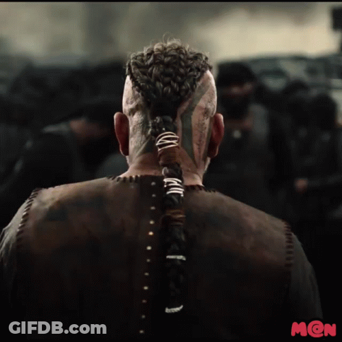 A Man With A Braided Ponytail And A Tattoo On His Face Is Standing In Front Of A Crowd GIF