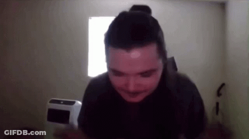 A Man With A Bun On His Head Is Standing In Front Of A Window In A Dark Room GIF