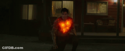 A Man With A Burning Heart On His Chest Stands In Front Of A House GIF