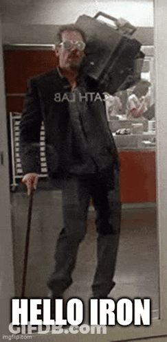 A Man With A Cane Is Carrying A Suitcase On His Shoulders And Says Hello Iron GIF