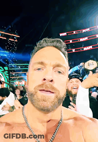 A Man With A Chain Around His Neck Holds Up A Wrestling Championship Belt GIF