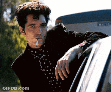 A Man With A Cigarette In His Mouth Leaning On A Car Door GIF