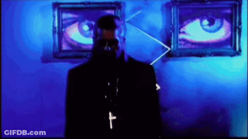 A Man With A Cross Around His Neck Is Standing In Front Of Two Large Eyes GIF