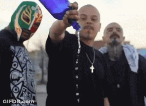 A Man With A Cross Necklace Pours Water Into Another Man 'S Face GIF