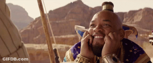 A Man With A Crown On His Head Is Smiling With His Hands On His Chin GIF