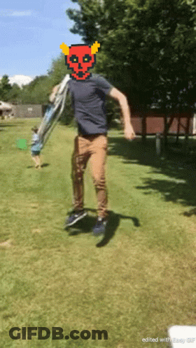A Man With A Devil Mask On His Head Is Jumping In The Grass GIF
