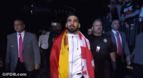 A Man With A Flag Around His Neck Walks Through A Crowd GIF