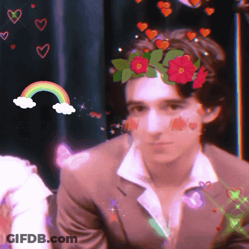 A Man With A Flower Crown On His Head And A Rainbow In The Background GIF