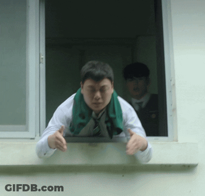 A Man With A Green Scarf Around His Neck Leans Out Of A Window GIF