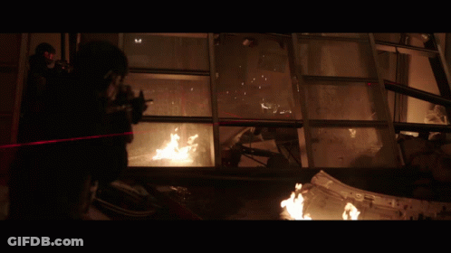 A Man With A Gun Is Standing In Front Of A Window With A Fire Coming Out Of It GIF