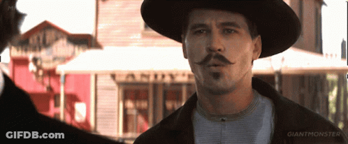 A Man With A Hat And Mustache Is Standing In Front Of A Building That Says Giant Monster GIF