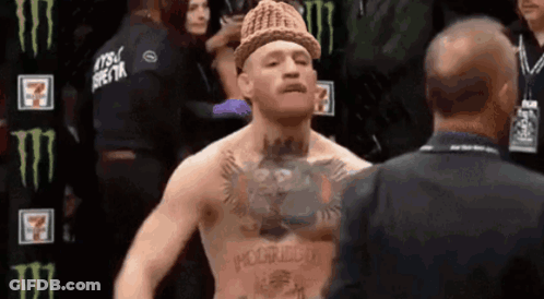 A Man With A Hat On His Head Is Talking To Another Man In A Suit . GIF