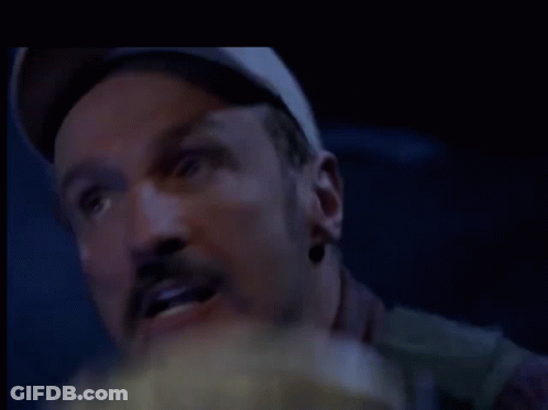 A Man With A Hat On Is Eating Popcorn In A Dark Room . GIF