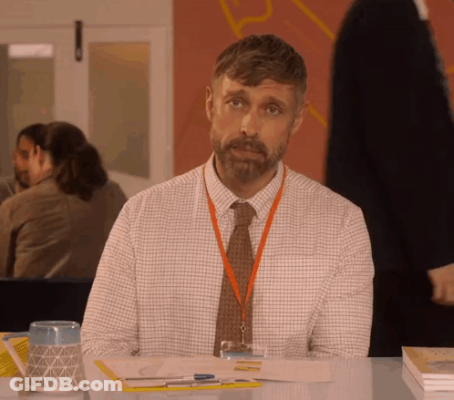 A Man With A Lanyard Around His Neck Sitting At A Desk GIF