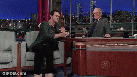 A Man With A Large Foot Is Sitting At A Table With A Man . GIF