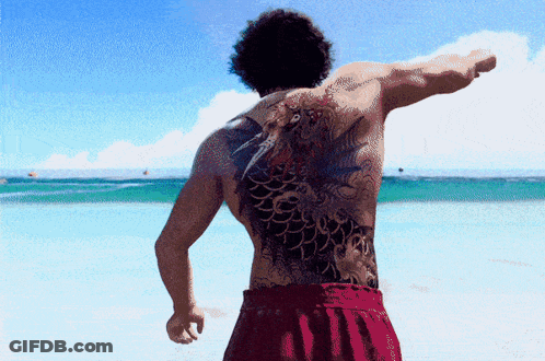 A Man With A Large Tattoo On His Back Is Standing On A Beach GIF