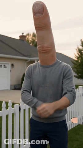 A Man With A Large Thumb On His Head Stands In Front Of A White Picket Fence GIF