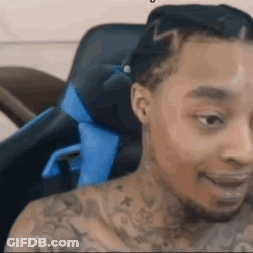 A Man With A Lot Of Tattoos Is Sitting In A Chair . GIF