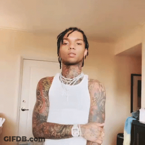 A Man With A Lot Of Tattoos Is Wearing A White Tank Top With His Arms Crossed GIF