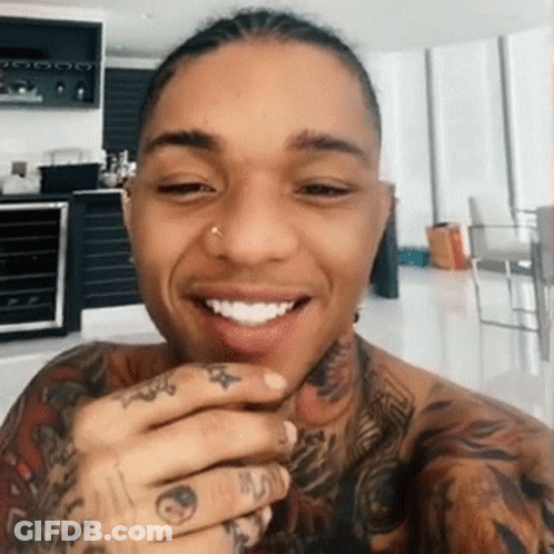 A Man With A Lot Of Tattoos On His Arms And Neck Is Smiling . GIF